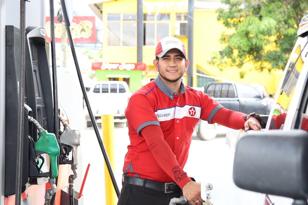 Cheerful gas station attendant refueling a car during the day.